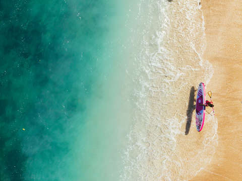 Aerial view of a surfer beside a sapphire blue sea