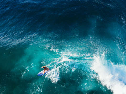 Aerial view of a surfer riding a sapphire blue wav