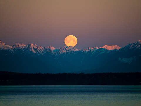 Full moon in Seattle setting over Olympic Mountains at sunrise