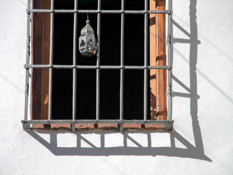 Tin lamp hangs from iron window work