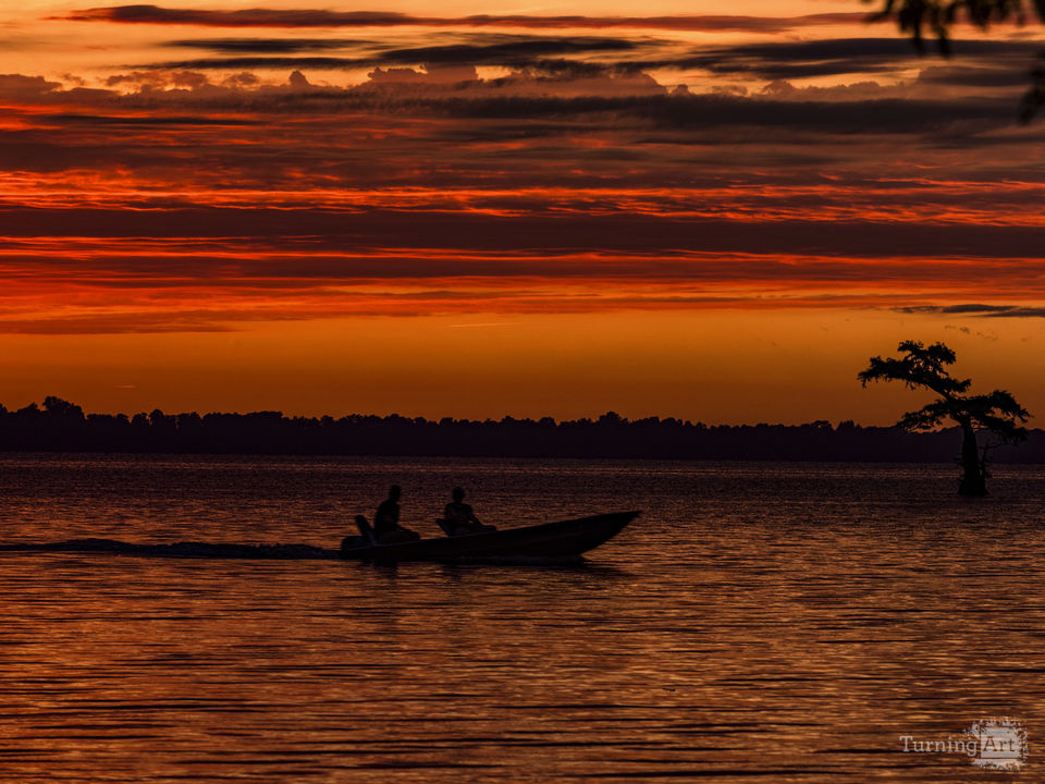 Fishermen returning to the bank in silhouette against an orange sky