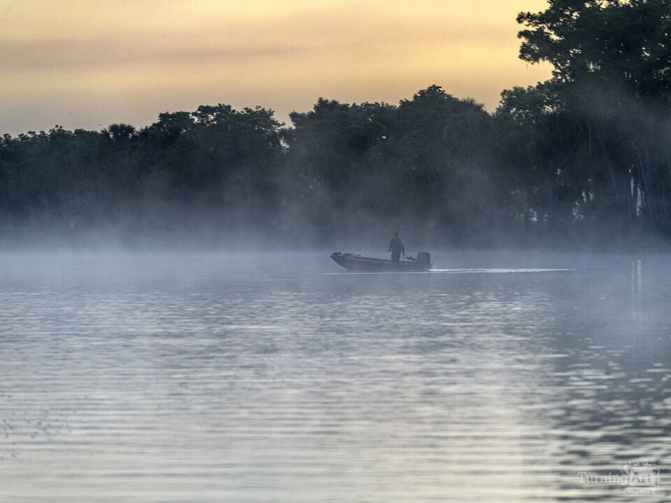 Fisherman in his boat during a foggy sunrise