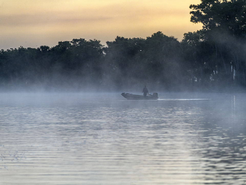 Fisherman in his boat during a foggy sunrise